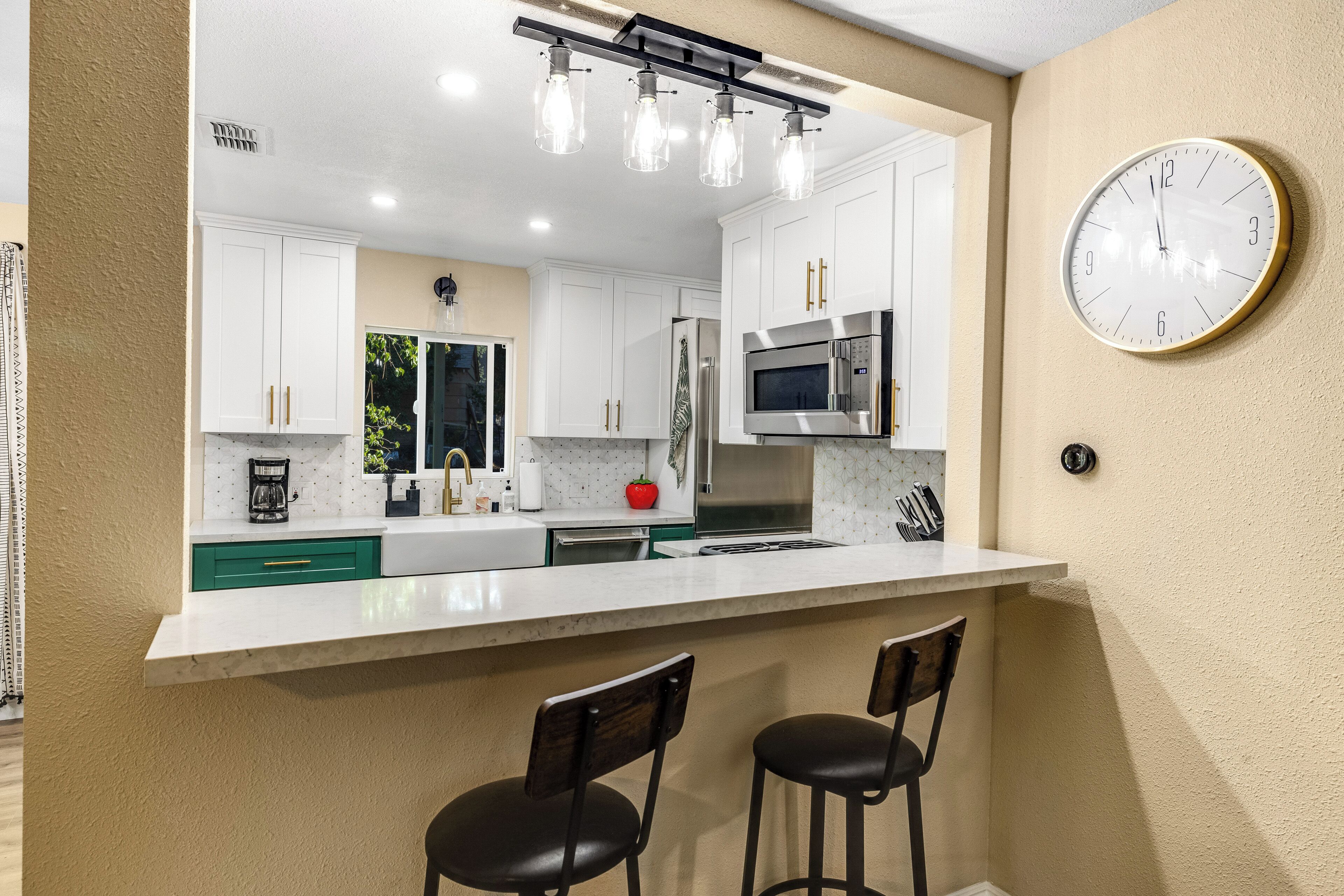 A modern kitchen with white cabinets, a stainless steel microwave, and a bar area with two stools.