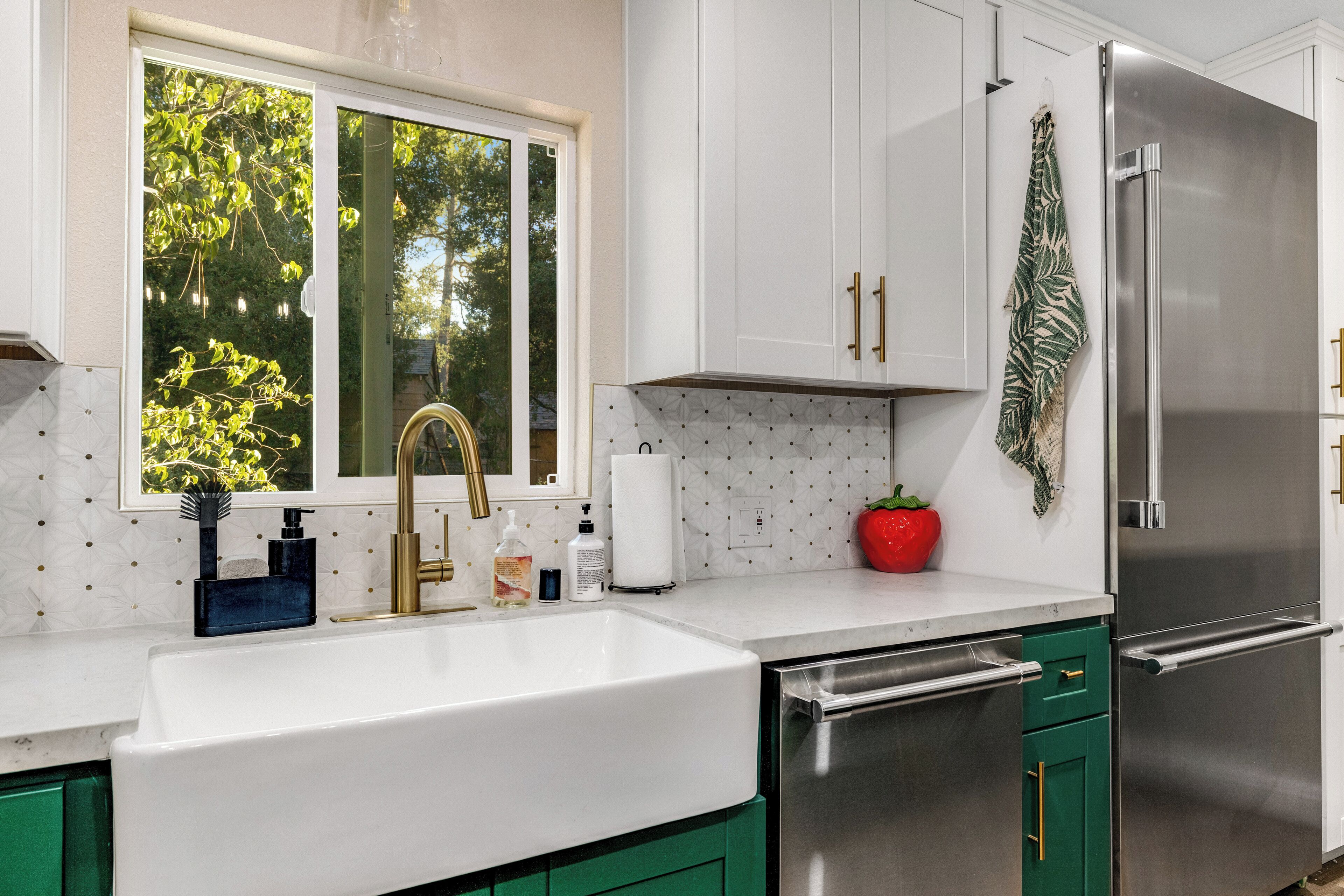 A modern kitchen with white cabinets, a stainless steel refrigerator, and a window with a view of trees.