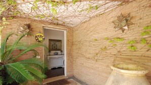 Una habitación pequeña y cerrada con pared de ladrillo, una planta en maceta, un jarrón grande y una puerta que da a otra habitación.