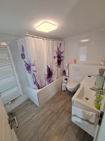 A modern bathroom with a shower curtain, toilet, sink, and a towel rack.. Cityapartment +terrace up to 4 persons Neuwied city center Rheinprominade