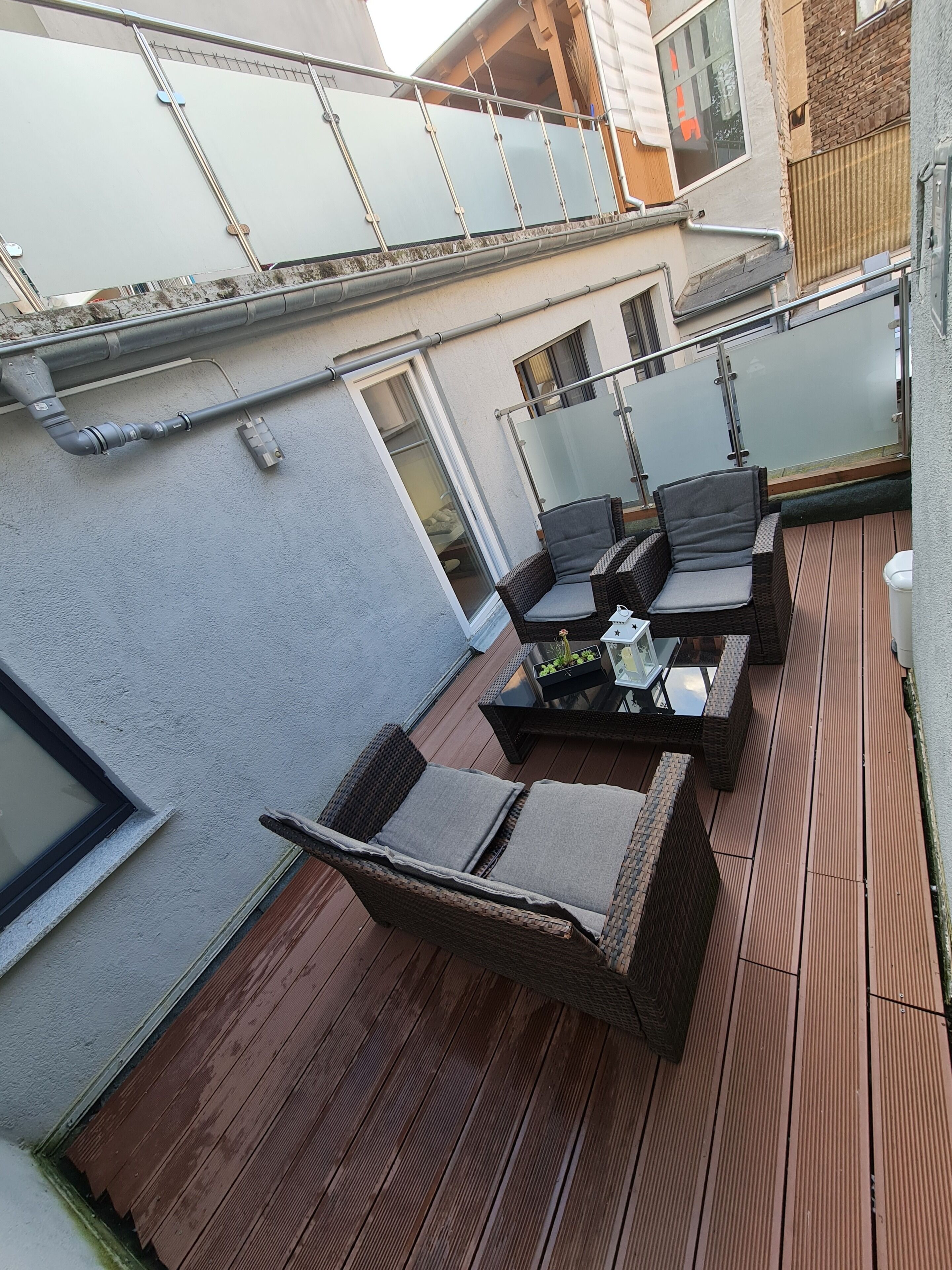 Una terraza en la azotea con mobiliario de mimbre, una mesa de vidrio y vistas a edificios cercanos.