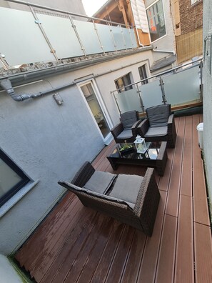 A rooftop patio with wicker furniture, a glass table, and a view of neighboring buildings. - Cityapartment +terrace up to 4 persons Neuwied city center Rheinprominade (Neuwied)