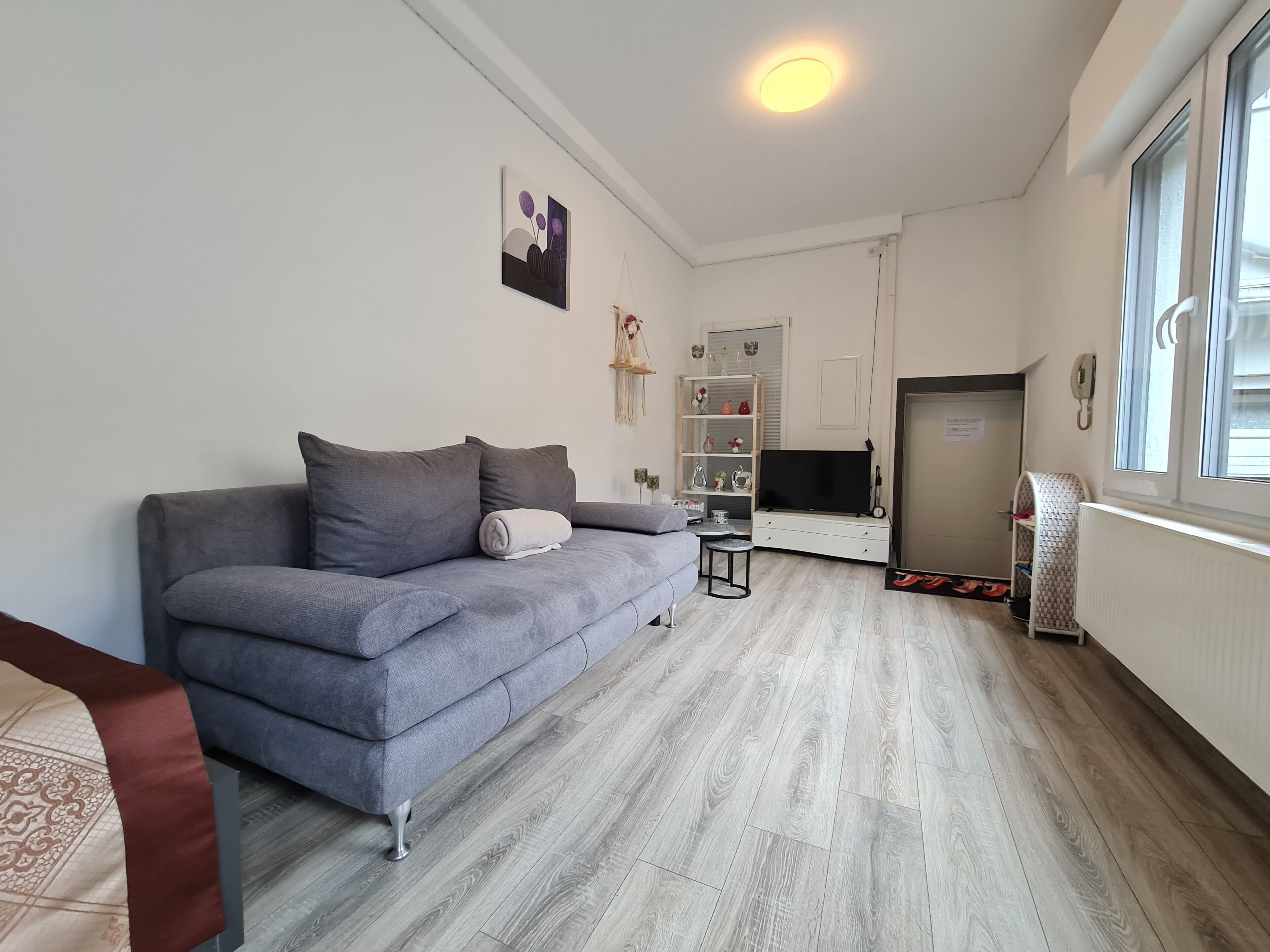 Ein Wohnzimmer mit grauem Sofa, einem kleinen Tisch, einem Fernseher und einer Heizung.
