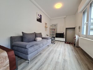 A living room with a grey sofa, a small table, a TV, and a radiator. - Cityapartment +terrace up to 4 persons Neuwied city center Rheinprominade (Neuwied)