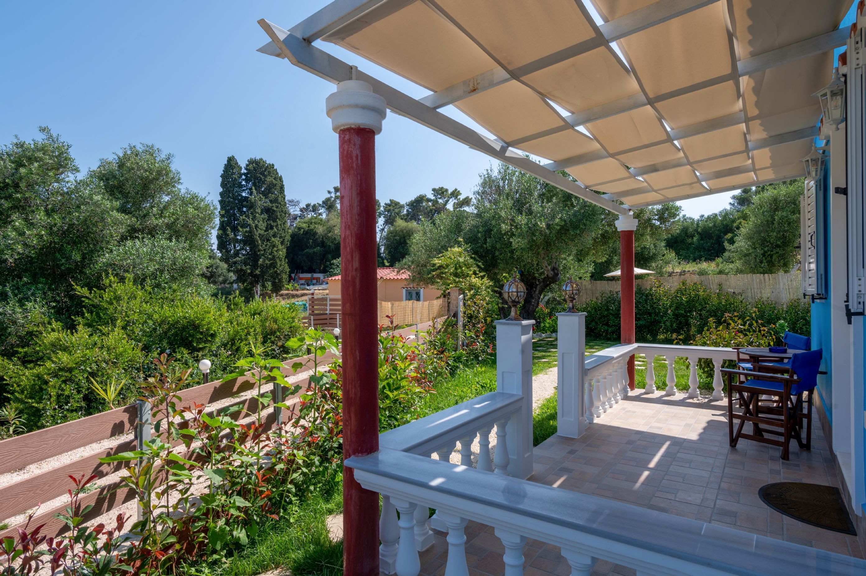 A covered outdoor area with a terrace, white balustrade, and a view of a garden and trees.