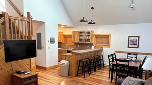 Una sala de estar moderna con piso de madera, un televisor de pantalla plana, una mesa de centro de madera, un sofá marrón y un comedor con mesa y sillas.