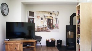 Een woonkamer met een flatscreen televisie, een houten tv-meubel, een schilderij van een straatbeeld, een open haard en een boekenkast.