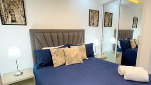 Een moderne slaapkamer met een groot bed, een nachtkastje, een spiegel en wanddecoratie.