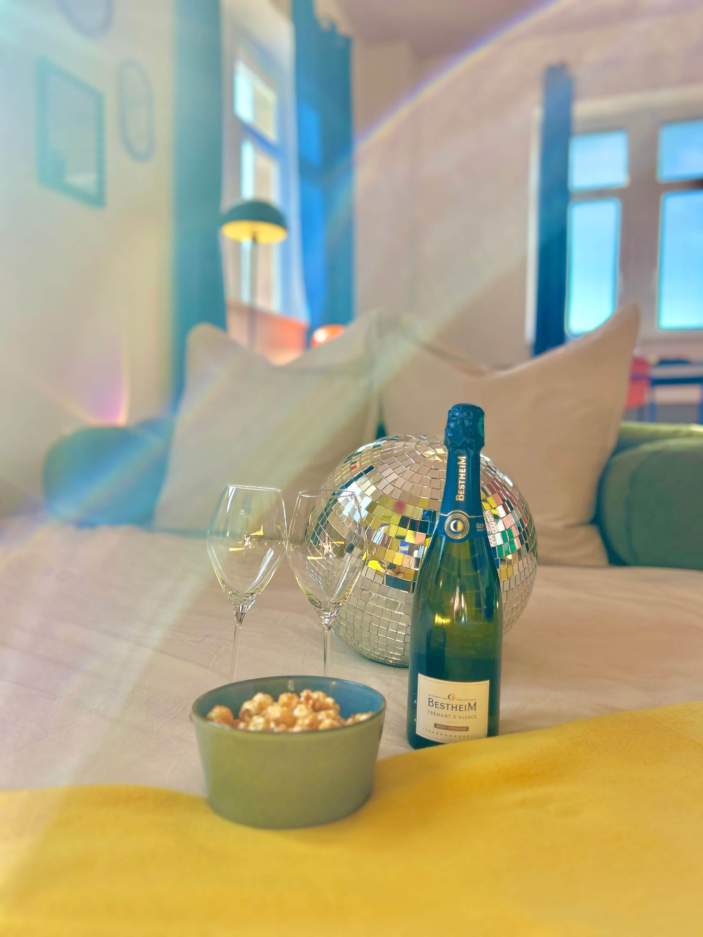 A room with a bed, a disco ball, two wine glasses, a bottle of champagne, and a bowl of popcorn.