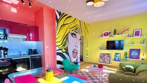 A modern living space with a vibrant color scheme, a kitchen area, a dining table with colorful chairs, a large wall mural, and a cozy seating area with a green sofa. - La Belle Breisach - PopArty - Colmar/Germany (Volgelsheim)