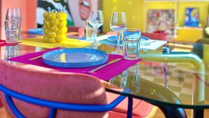 A dining table with colorful tableware and glasses, a yellow sculpture, and a vibrant mural in the background. - La Belle Breisach - PopArty - Colmar/Germany (Volgelsheim)