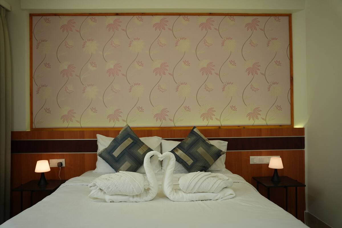 A hotel room with a bed, two pillows, two nightstands, and a wall with floral wallpaper.