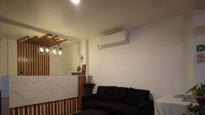 A modern living room with a reception desk, a black sofa, a wooden floor, and a ceiling light fixture. - The R One (Hulhumalé)