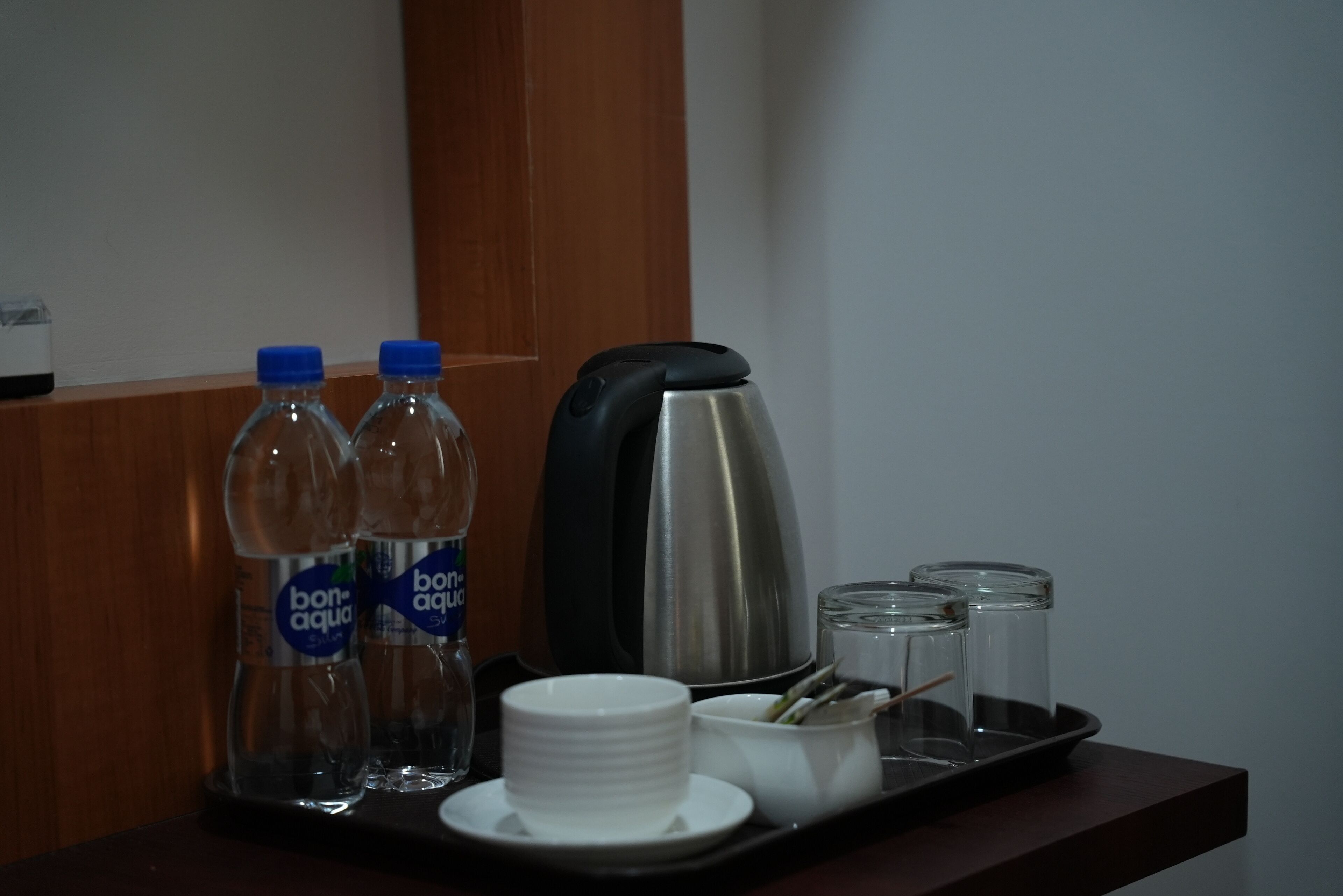 A tray with two water bottles, a coffee maker, and a set of white cups and saucers.