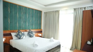 A hotel room with a large bed, a wooden headboard, a desk, and a window with curtains. - The R One (Hulhumalé)