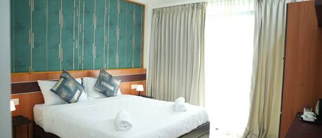 A hotel room with a large bed, a wooden headboard, a desk, and a window with curtains.