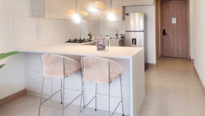Een moderne keuken met een centraal eiland, barstoelen, hanglampen en een koelkast.