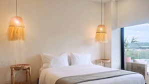 Een moderne slaapkamer met een groot bed, twee hanglampen, een klein nachtkastje en uitzicht op de omgeving.
