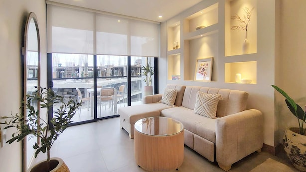 Een moderne woonkamer met een bank, een ronde salontafel en een groot raam met uitzicht op de stad.