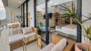 Een moderne woonkamer met rieten meubels, een glazen salontafel en uitzicht op bouwactiviteiten.