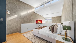 Ein modernes Schlafzimmer mit einem großen Bett, einem an der Wand montierten Fernseher und einem Fenster mit Blick zum Himmel.
