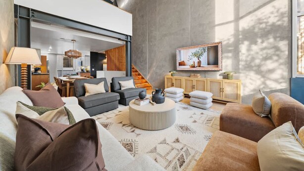 Ein modernes Wohnzimmer mit hohen Decken, einem Essbereich und einem an der Wand befestigten Fernseher.