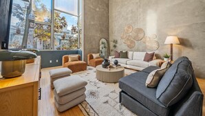 Ein modernes Wohnzimmer mit großem Fenster, rundem Couchtisch und grauem Sofa.