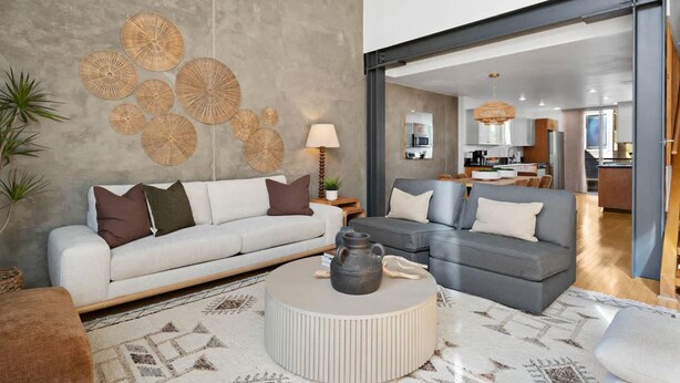 Un soggiorno moderno con un divano e una poltrona grigi, e un tavolino rotondo. Sullo sfondo a sinistra, un pannello decorativo con motivi circolari e una pianta.