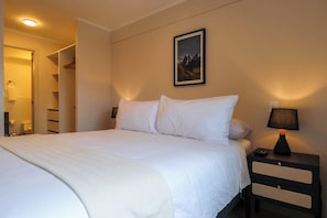 Ein ordentlich bezogenes Bett mit weißen Laken, einer Nachttischlampe und einem gerahmten Bild an der Wand.
