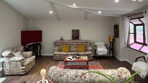Un salon comprenant un ensemble de canapés, un téléviseur rouge, un tableau et une fenêtre avec des rideaux.