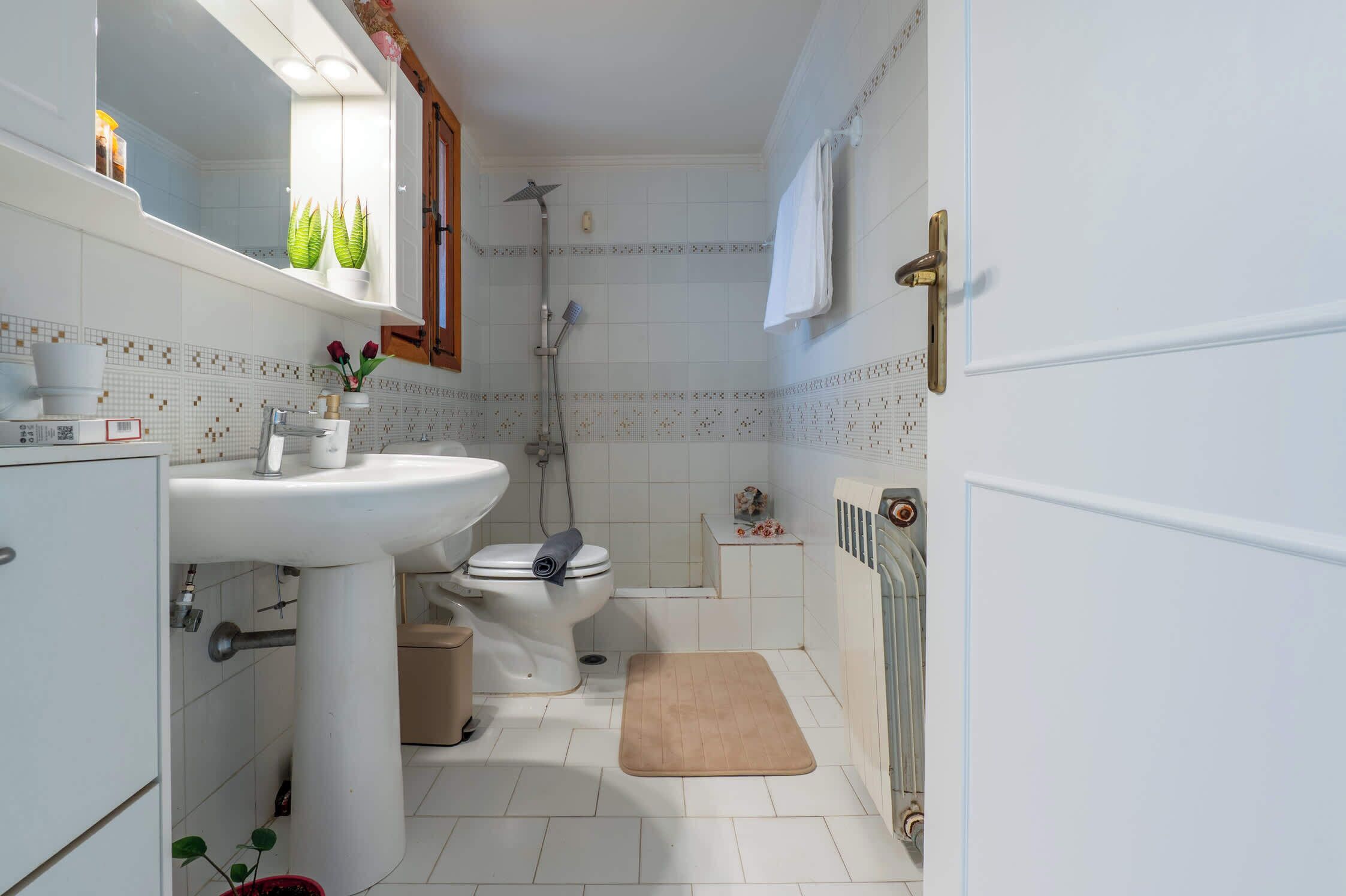 Une petite salle de bain avec un lavabo, des toilettes et une douche, le tout de couleur blanche.
