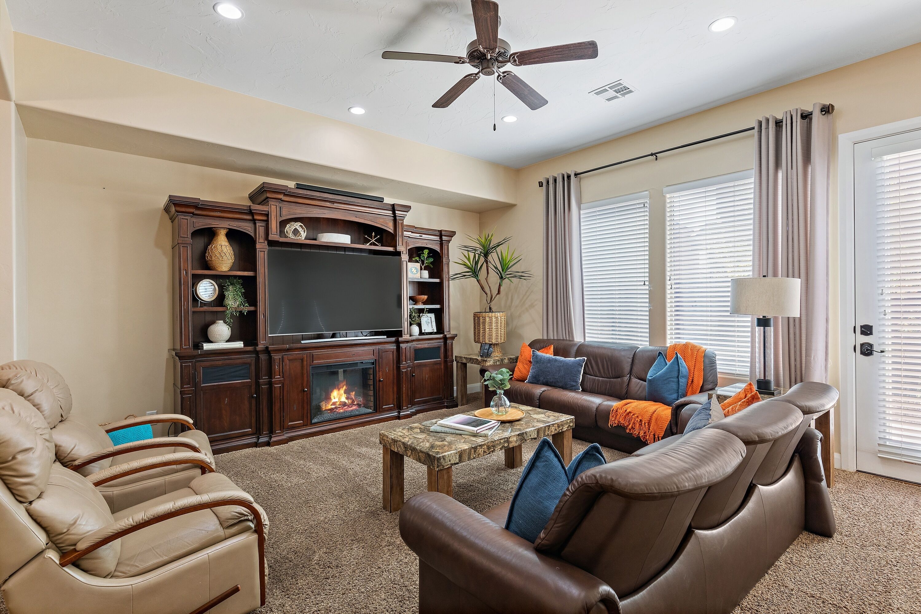 A living room with a fireplace, leather sofas, a coffee table, and a ceiling fan.