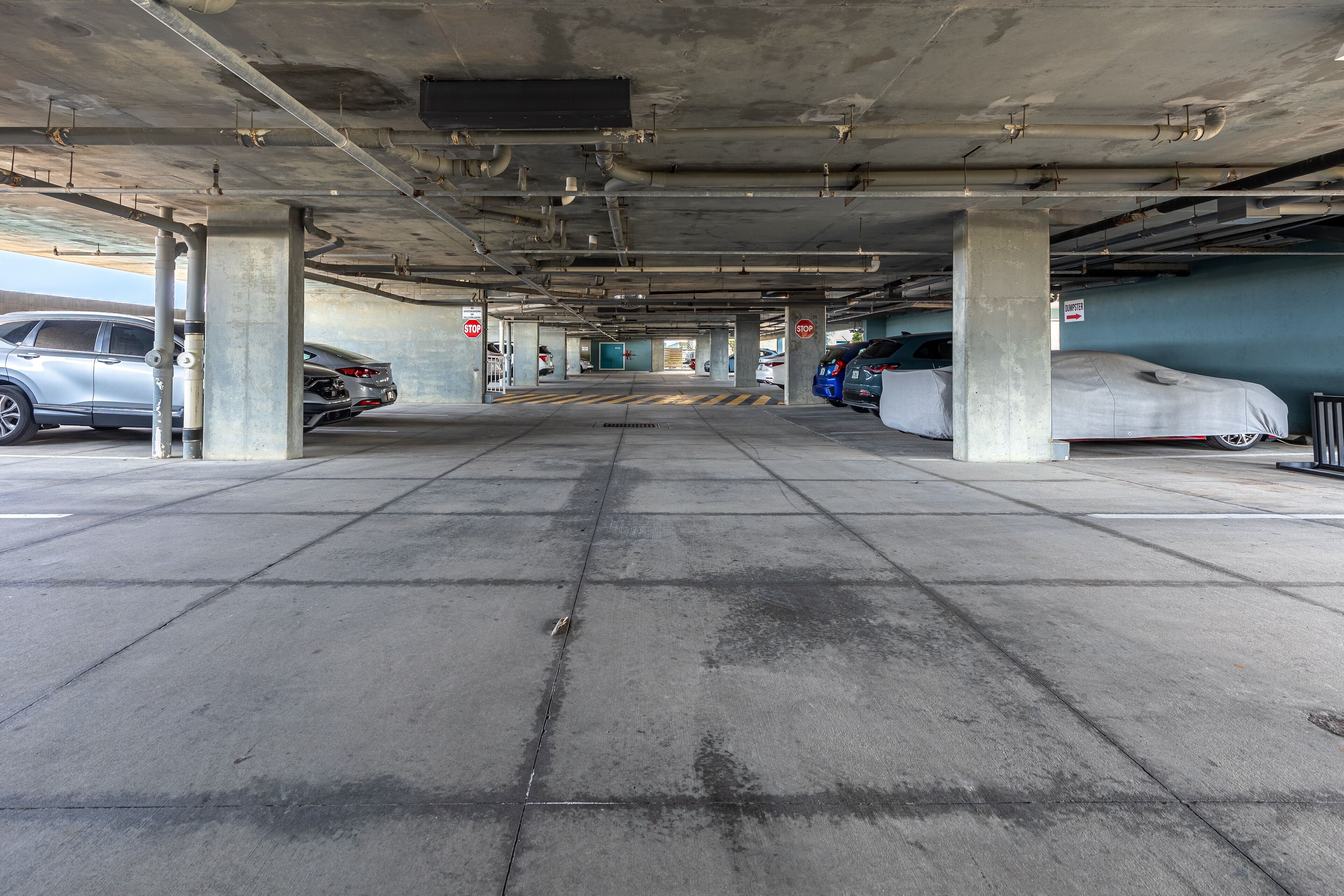 An underground parking garage with concrete pillars, a central walkway, and parked cars.