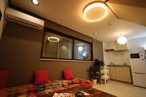 Un salon confortable avec un canapé, une table à manger, un coin cuisine et une fenêtre équipée de stores.