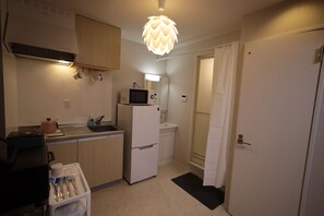 Une cuisine compacte équipée d’un four à micro-ondes, d’un réfrigérateur et d’un évier. On y trouve un luminaire au plafond et une porte donnant accès à la salle de bain.
