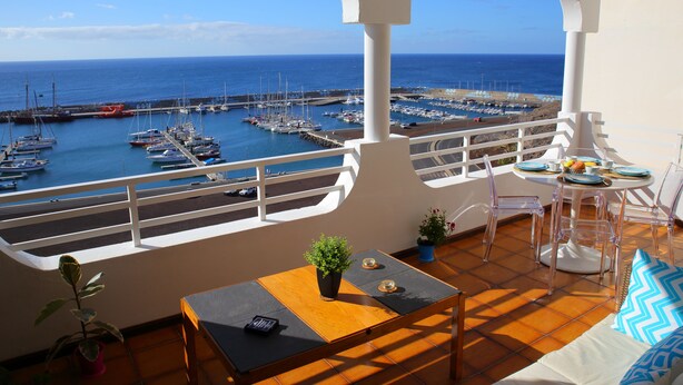 Un balcon donnant sur un port de plaisance, une table avec des chaises et une plante en pot.