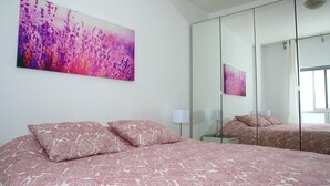 Une chambre à coucher avec un lit, deux oreillers, une table de chevet, une lampe et un grand miroir.