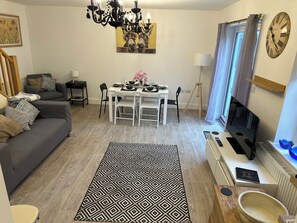 A modern living room with a dining area, a chandelier, a clock, and a television. - Bright Modern Entire Open-Plan Home –with off street Parking Included (Exeter)