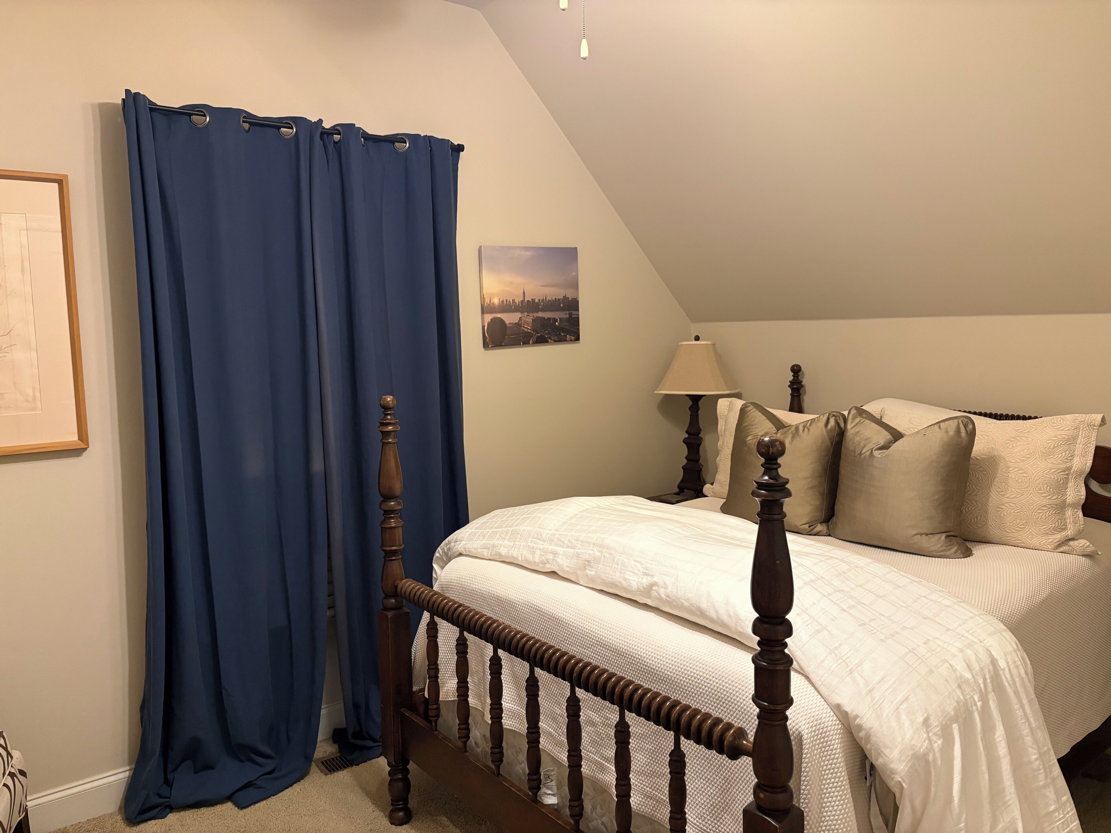 A bedroom with a wooden bed frame, a white bedspread, and a blue curtain.