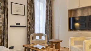 Ein modernes Wohnzimmer mit einer Couch, einem Sessel, einem kleinen Tisch und einem Fernseher.