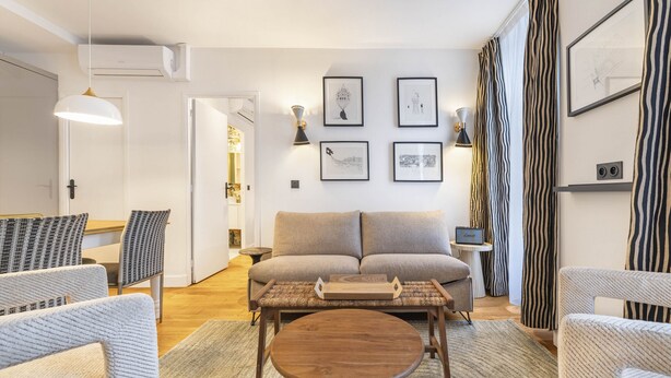 Ein modernes Wohnzimmer mit einer Couch, zwei Sesseln, einem Couchtisch und einer TV-Konsole mit einem kleinen Tisch und einer Lampe.