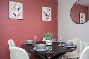 A dining area with a round table set for four, framed artwork on the walls, and a mirror on the wall. - Vacant Nest  | Cleveland Close | Central | Parking (County Durham)