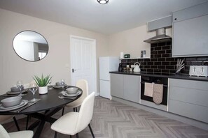 A modern kitchen with grey cabinets, a black countertop, and a round mirror on the wall.