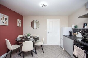 A compact kitchen with a dining area, a white door, and a small refrigerator.