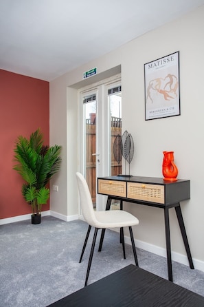 A room with a white chair, a black and wooden desk, a red vase, a framed artwork, and a potted plant. - Vacant Nest  | Cleveland Close | Central | Parking (County Durham)