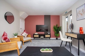 A modern living room with a flat-screen TV, a black coffee table, wicker furniture, and a potted plant.