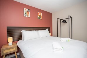 A neatly made bed with white linens, a bedside lamp, and a wall-mounted coat rack with hangers. - Vacant Nest  | Cleveland Close | Central | Parking (County Durham)