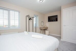 A bedroom with a bed, a bedside table, a mirror, a TV, and a door.