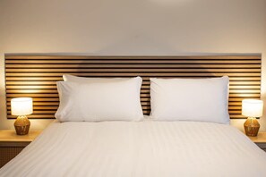 Une chambre d’hôtel avec une tête de lit en bois, deux oreillers blancs et deux lampes de chevet.