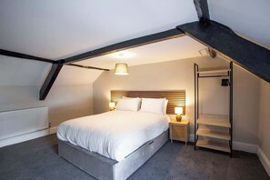 A bedroom with a sloped ceiling, a bed, bedside lamps, a wooden headboard, and a built-in shelf. - Vacant Nests | The Beulah | Town Centre | Starlink (Allendale Town)